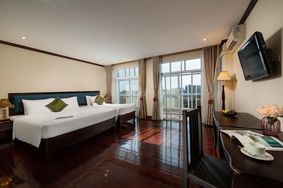 Une chambre d’hôtel avec un grand lit, un bureau, une télévision et une fenêtre avec des rideaux.