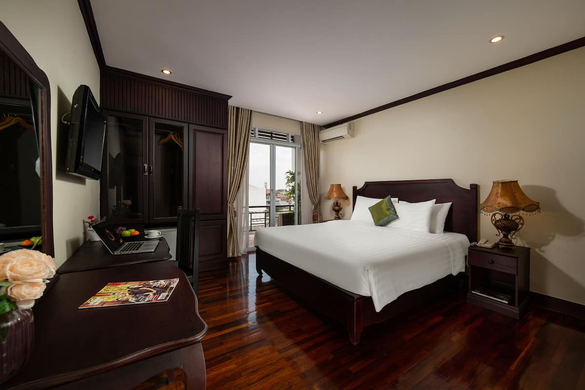 Une chambre d’hôtel avec un grand lit, un bureau avec un ordinateur portable, un vase de fleurs et une vue sur l’extérieur.