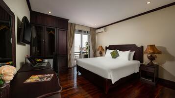 Habitación de hotel con una cama grande, un escritorio con una computadora portátil, un jarrón de flores y vistas al exterior.