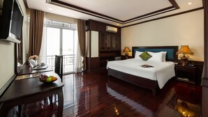 A hotel room with a large bed, a desk with a laptop and a bowl of fruit, a TV, and a window with curtains. - Vientiane Golden Sun Hotel & Spa (Vientiane)