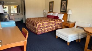 A hotel room with a bed, a desk, a chair, a small table, and a nightstand. - Claridge Inn (Waynesboro)