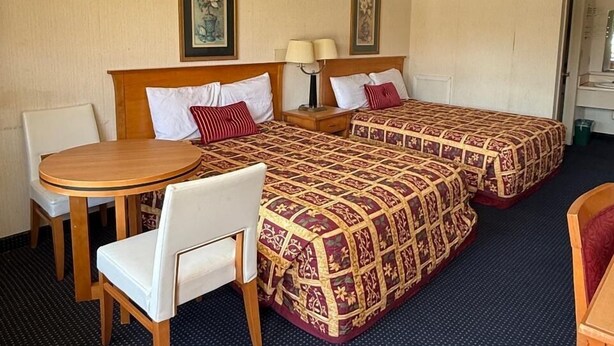 A hotel room with two beds, a round wooden table, and a chair. - Claridge Inn (Waynesboro)