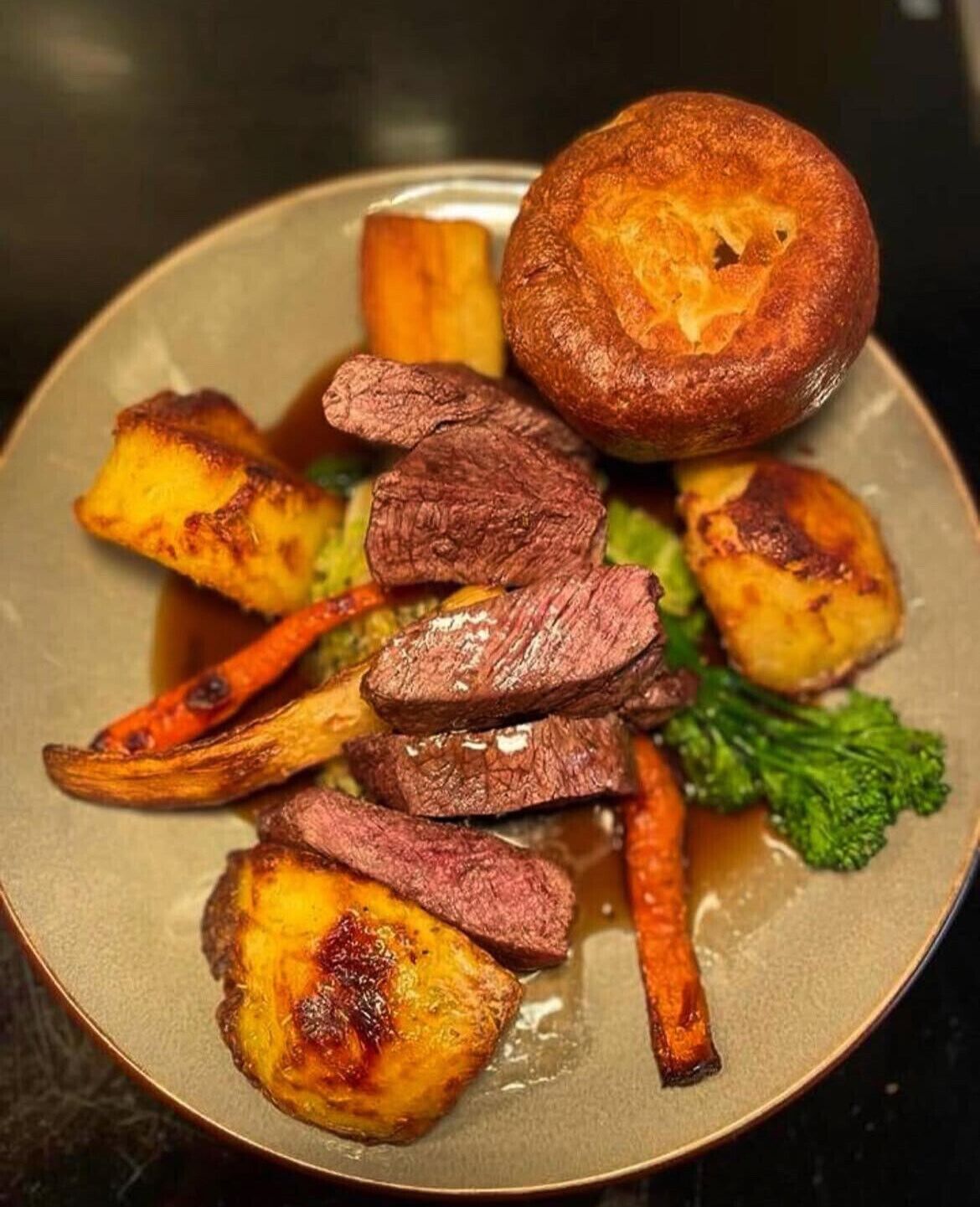 Un piatto di carne con fette di manzo, patate arrosto e uno Yorkshire pudding.