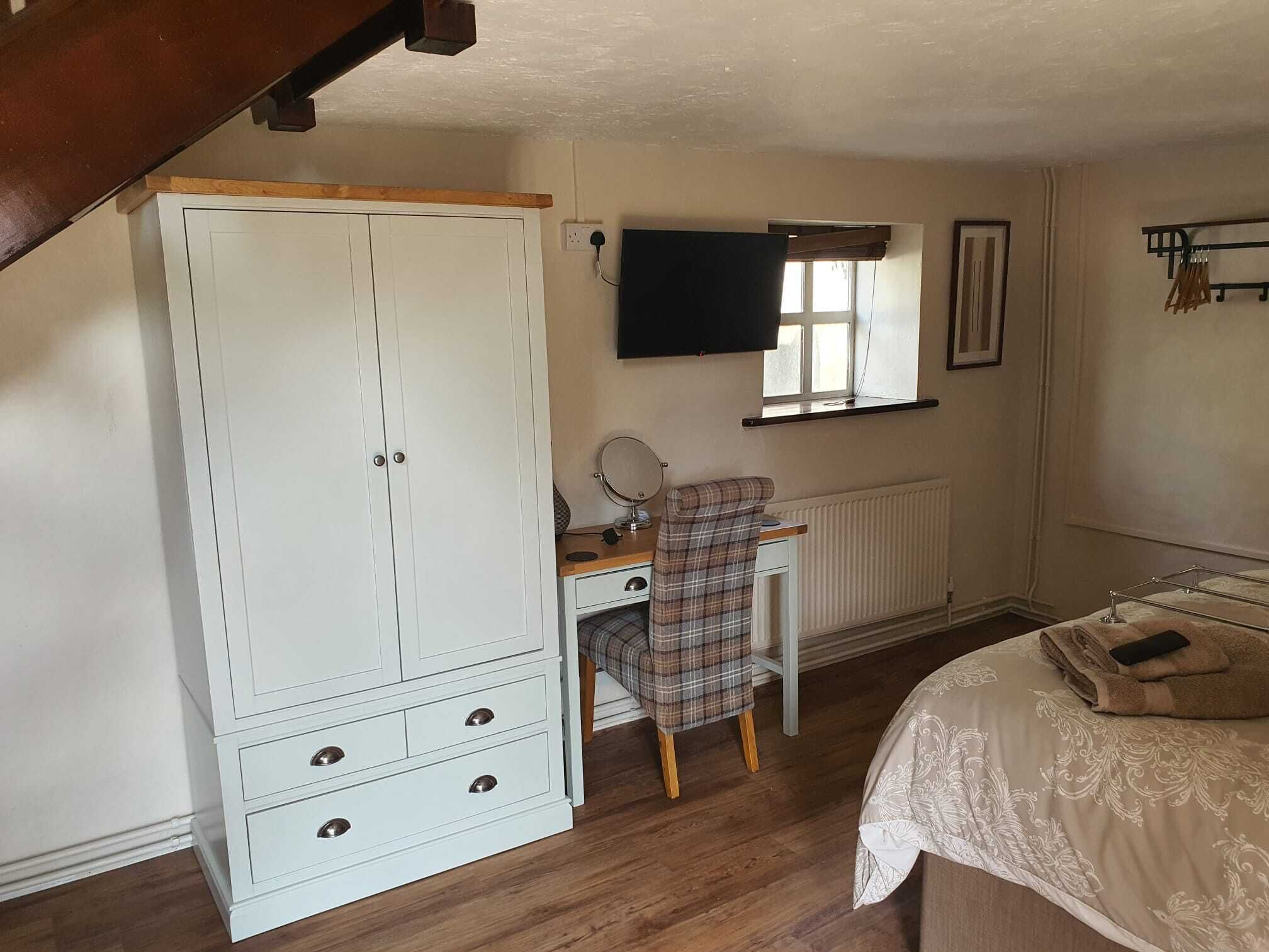 A bedroom with a large wardrobe, a desk with a chair, a bed, a window, and a radiator.