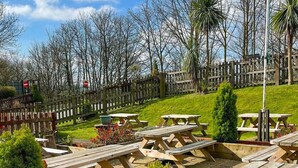 A picnic area with wooden tables and benches, surrounded by a wooden fence and trees. - The Lower Bell (Aylesford)