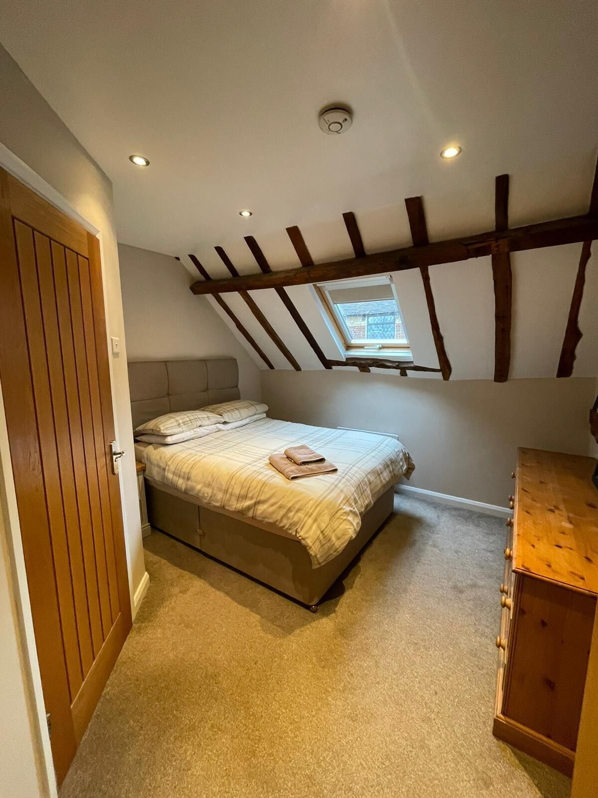 A bedroom with a sloped ceiling, a bed, a wooden wardrobe, and a small window.