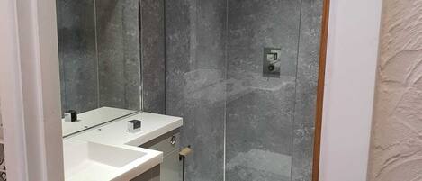 Un baño moderno con cabina de ducha de vidrio, un lavabo blanco y un inodoro.