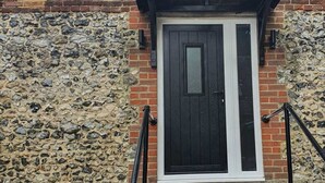 A stone facade with a black door and white trim, a small window above the door, and a set of concrete steps leading up to the entrance. - The Lower Bell (Aylesford)