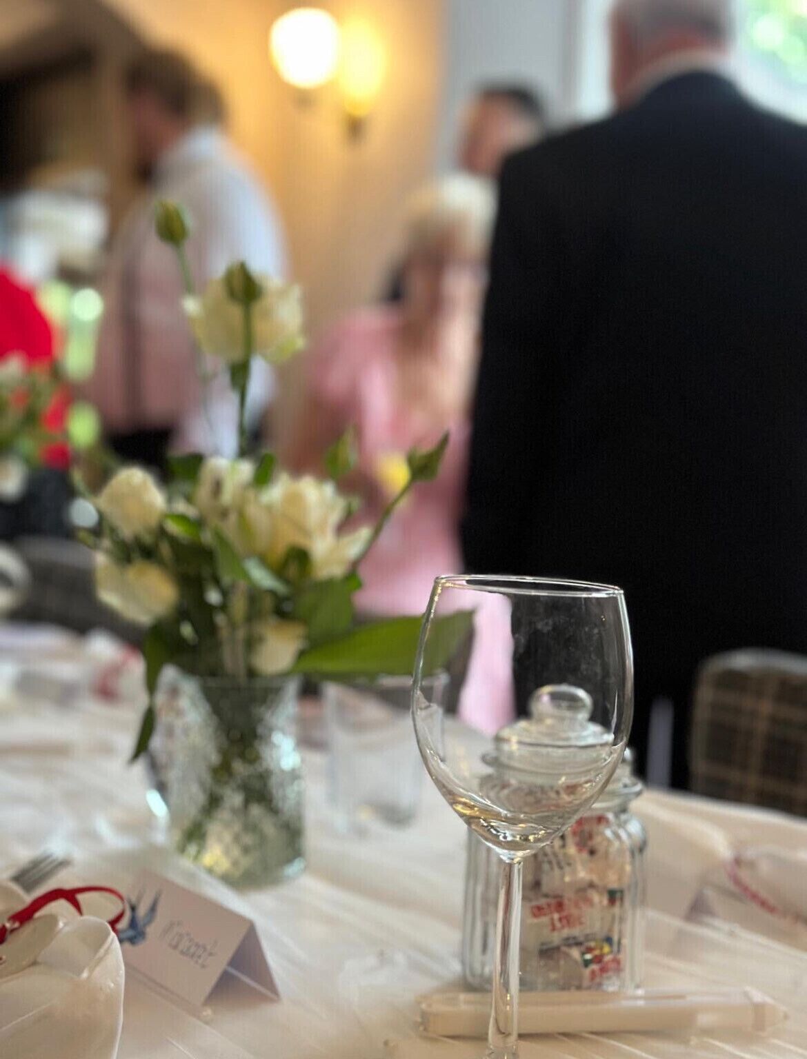 A table with a glass, a vase with flowers, and a small container.