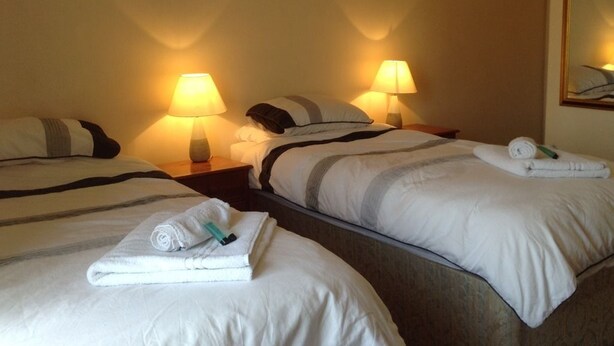 Een hotelkamer met twee bedden, elk voorzien van een kussen en een opgerolde handdoek. Op de nachtkastjes staan twee bedlampjes.