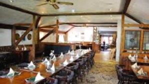 Een restaurant met lange gedeelde tafels, houten balken en een plafondventilator.