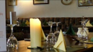 Een restaurantsetting met een menukaart, kaars en wijnkaraffen op de tafel.