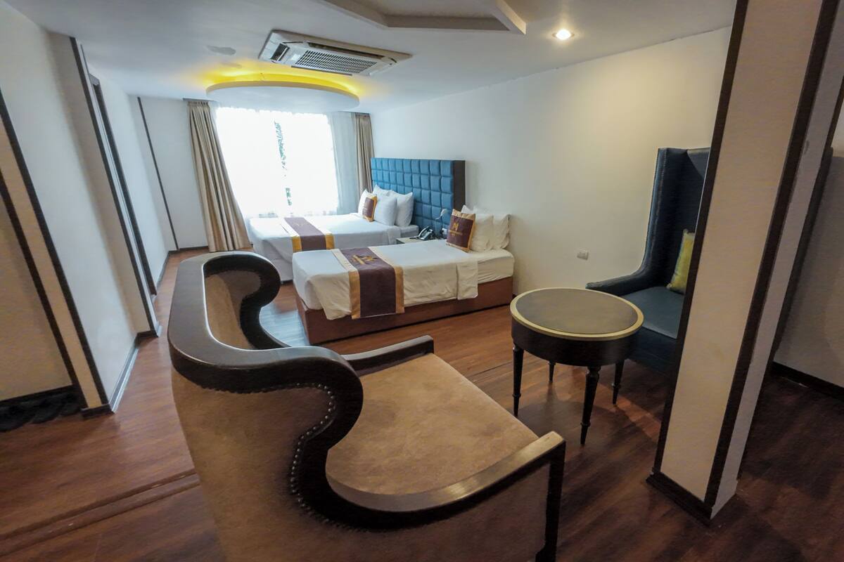 A hotel room with a large bed, a small round table, a curved chair, and a view of the outdoors.