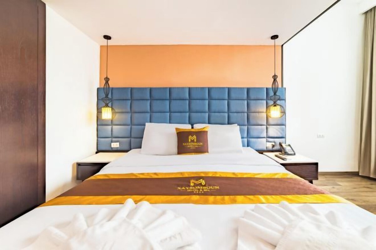 A hotel room with a large bed, a blue headboard, two bedside lamps, and a nightstand with a phone.