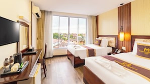 A hotel room with two beds, a desk with a flat-screen TV, a window with a view of buildings, and a wall-mounted air conditioner.