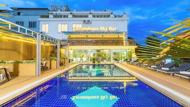 A hotel with a swimming pool, outdoor seating, and a well-lit entrance.