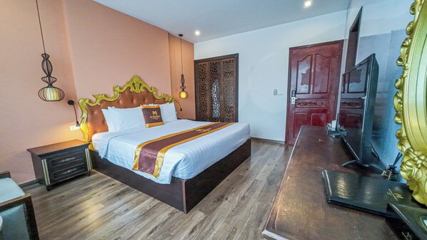 A bedroom with a large bed, wooden floor, a TV, and a decorative door.