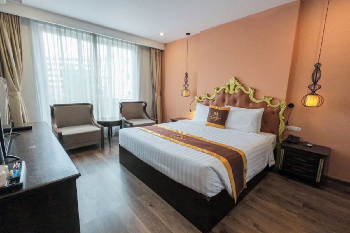 A hotel room with a large bed, two armchairs, a desk, and a nightstand.