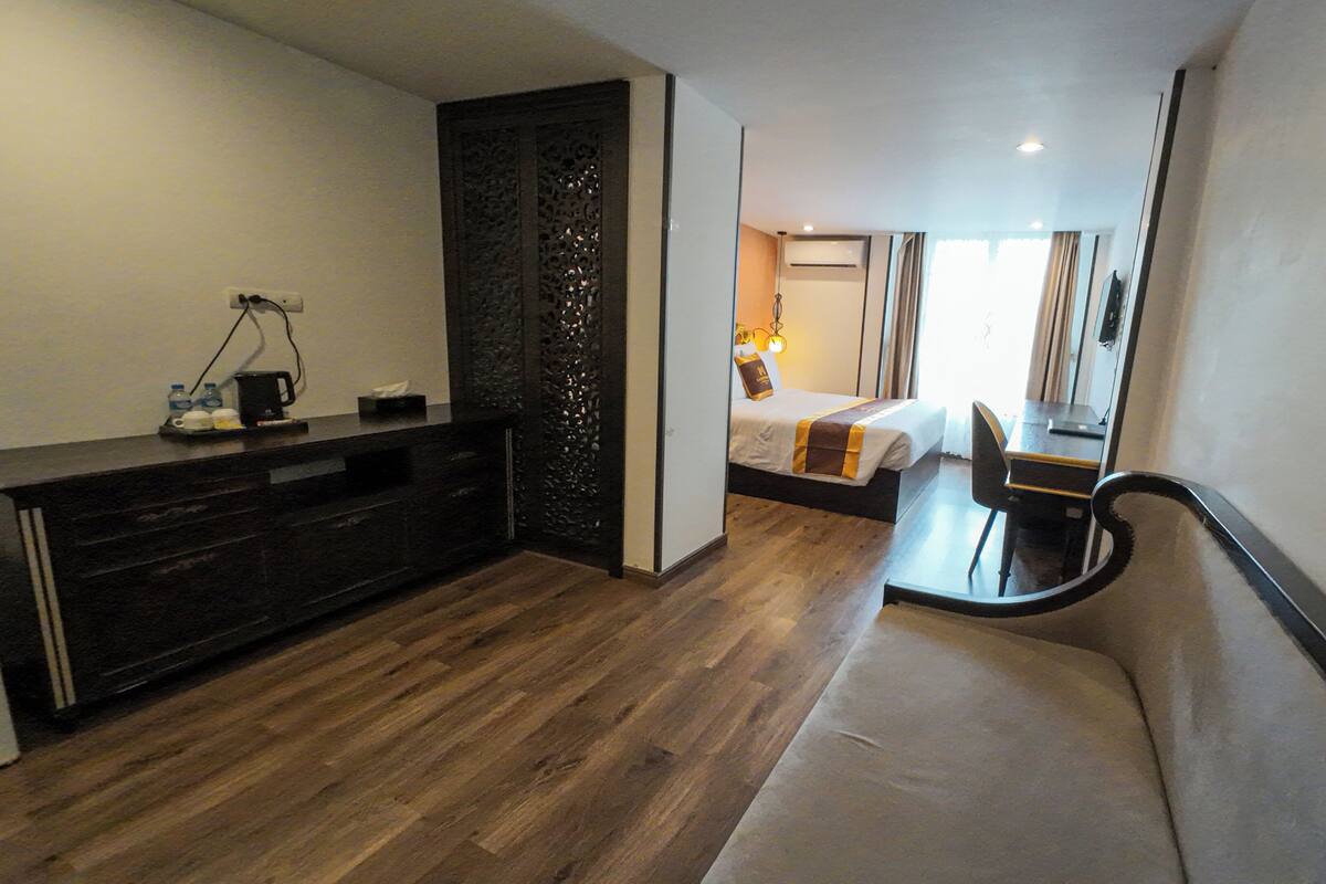 A hotel room with a wooden floor, a bed with a headboard, a desk, and a chair.