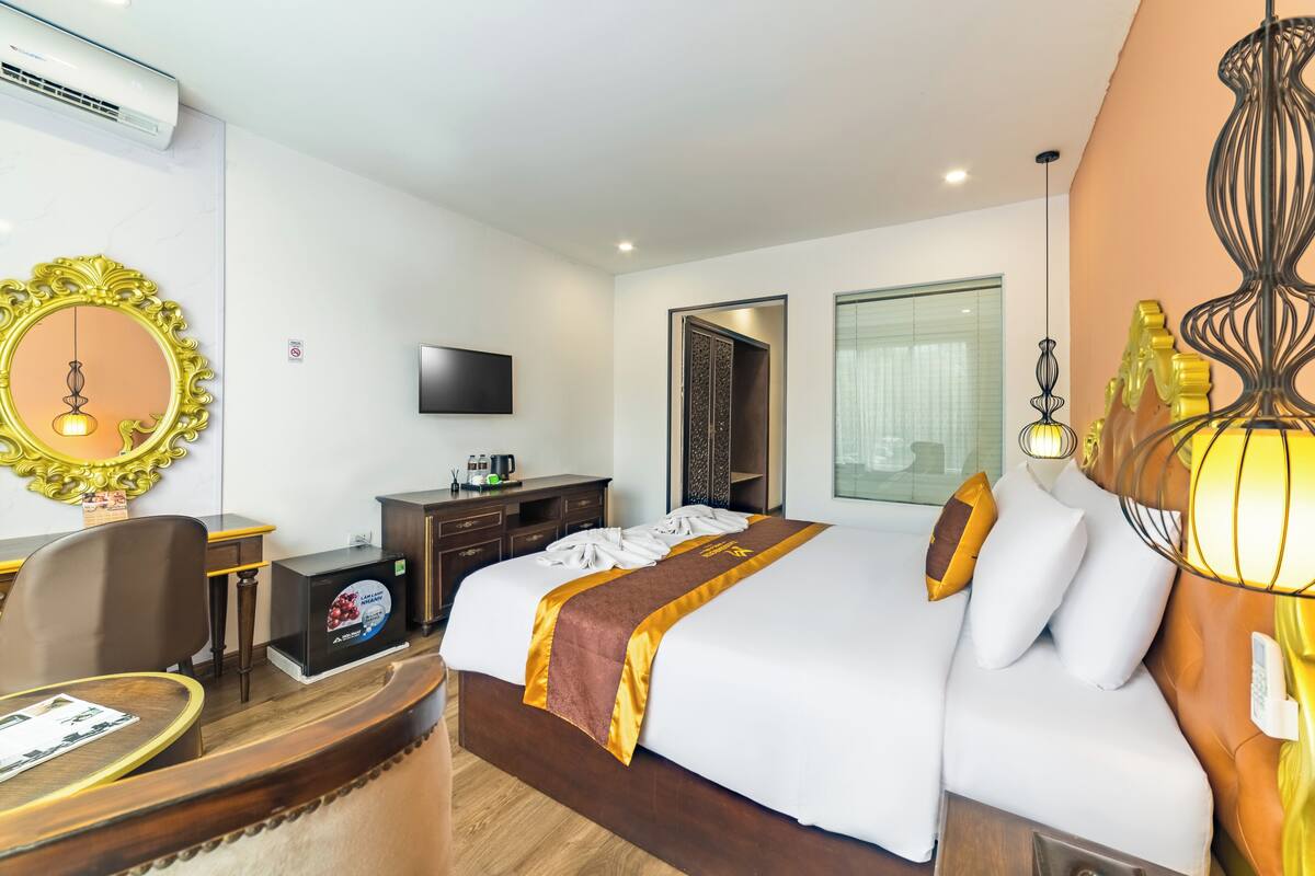 A hotel room with a large bed, a desk with a computer, a television, and a minibar.