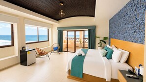 A hotel room with a bed, a desk, a chair, a view of the ocean, and a balcony.