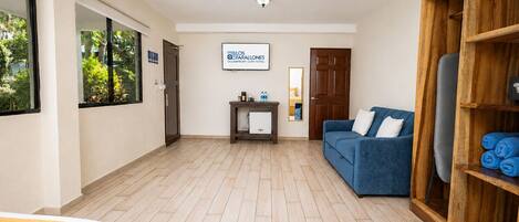 A hotel room with a wooden floor, a blue sofa, a wooden wardrobe, and a desk with a mirror.
