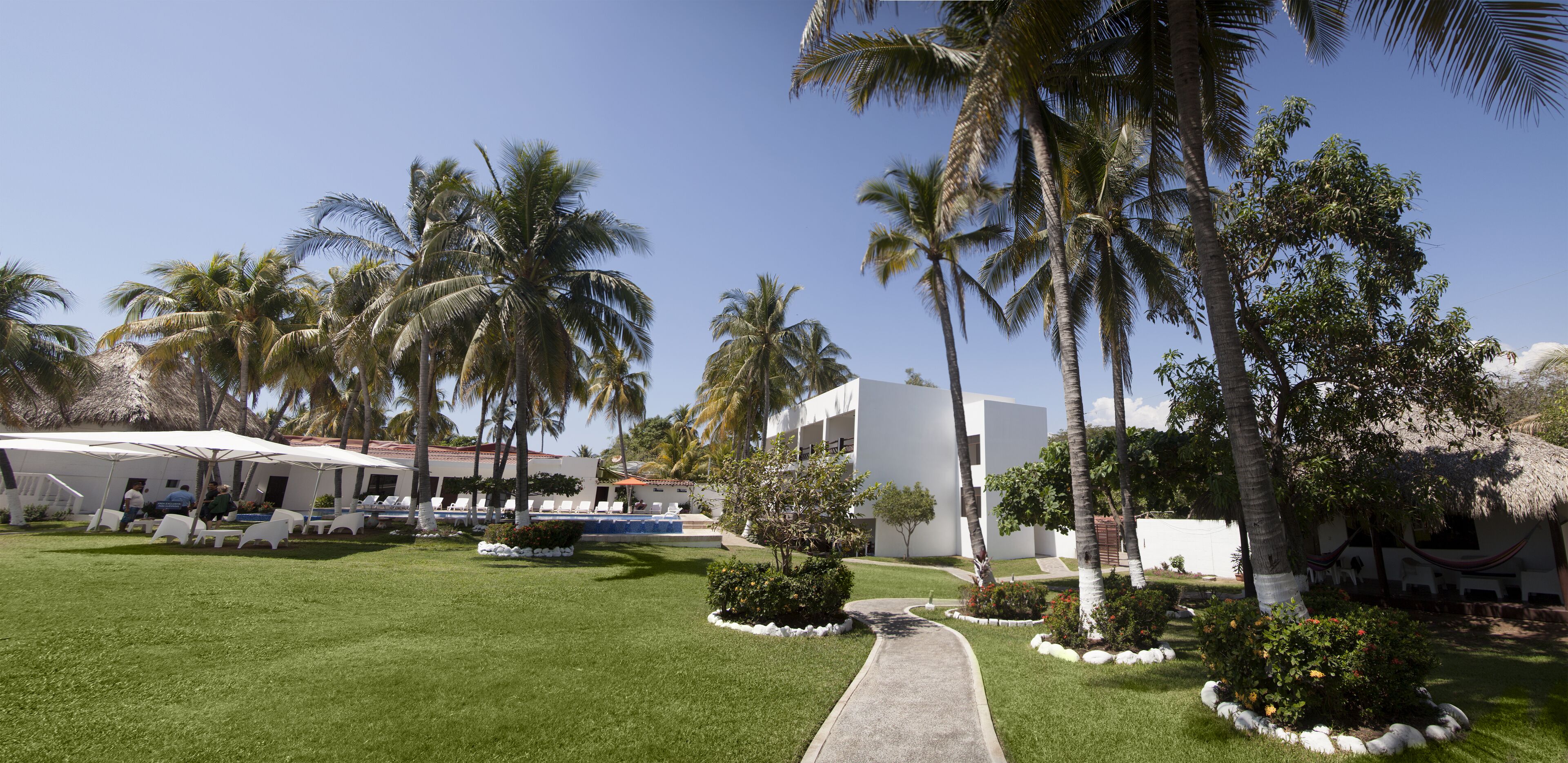 A resort with a pool, palm trees, and a well-maintained lawn.