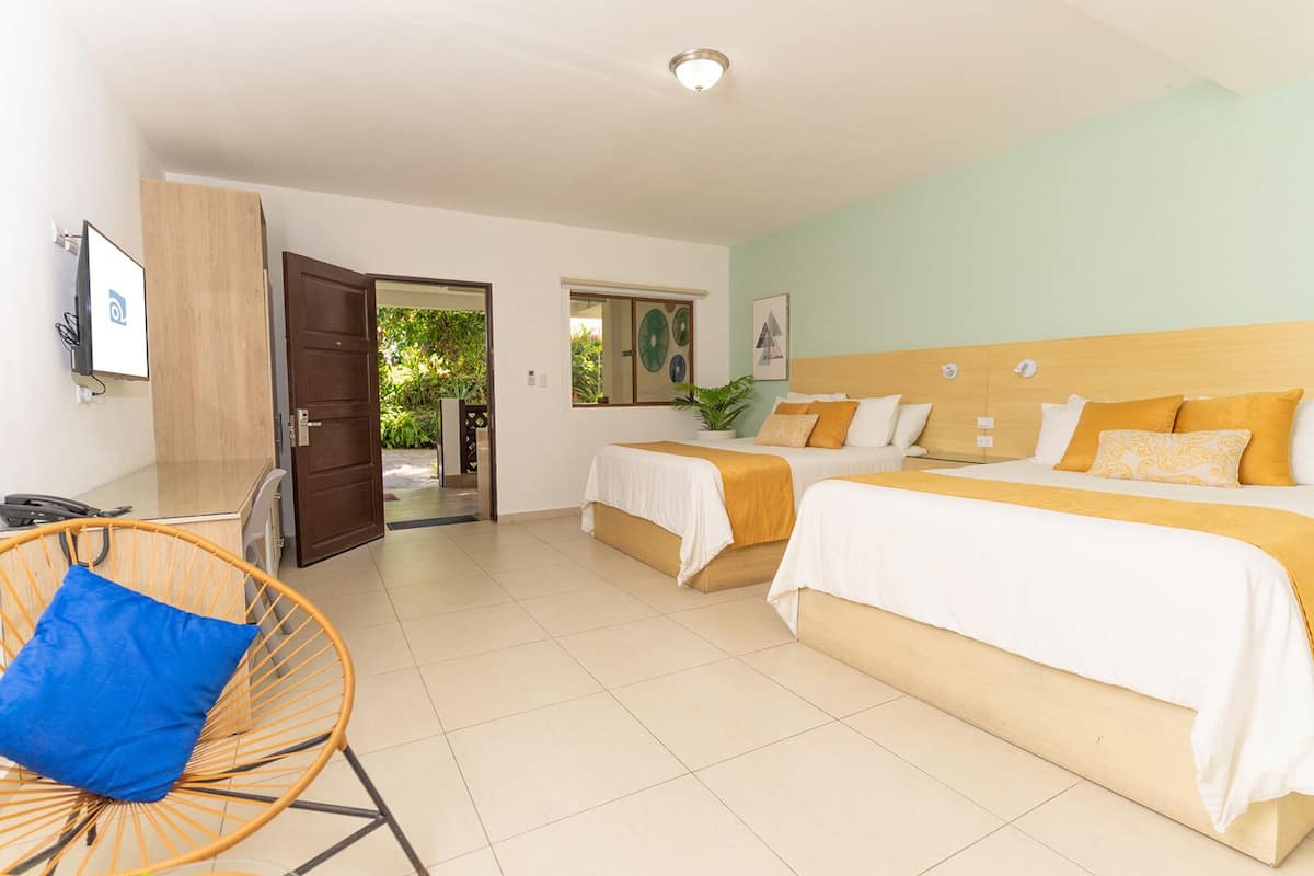 Habitación de hotel con dos camas, una silla, un escritorio y una puerta que da al exterior.