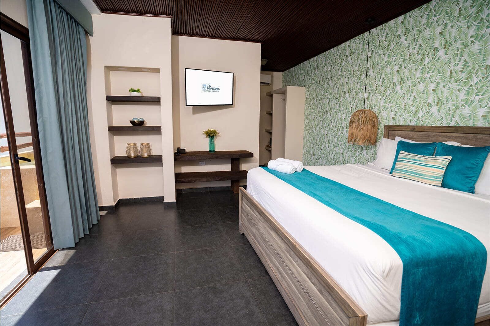 Une chambre d’hôtel moderne avec un grand lit, un téléviseur fixé au mur et une vue sur l’extérieur grâce à une porte-fenêtre coulissante.