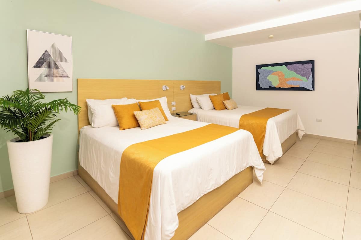 Una habitación de hotel con dos camas, una planta grande en maceta y obras de arte en las paredes.