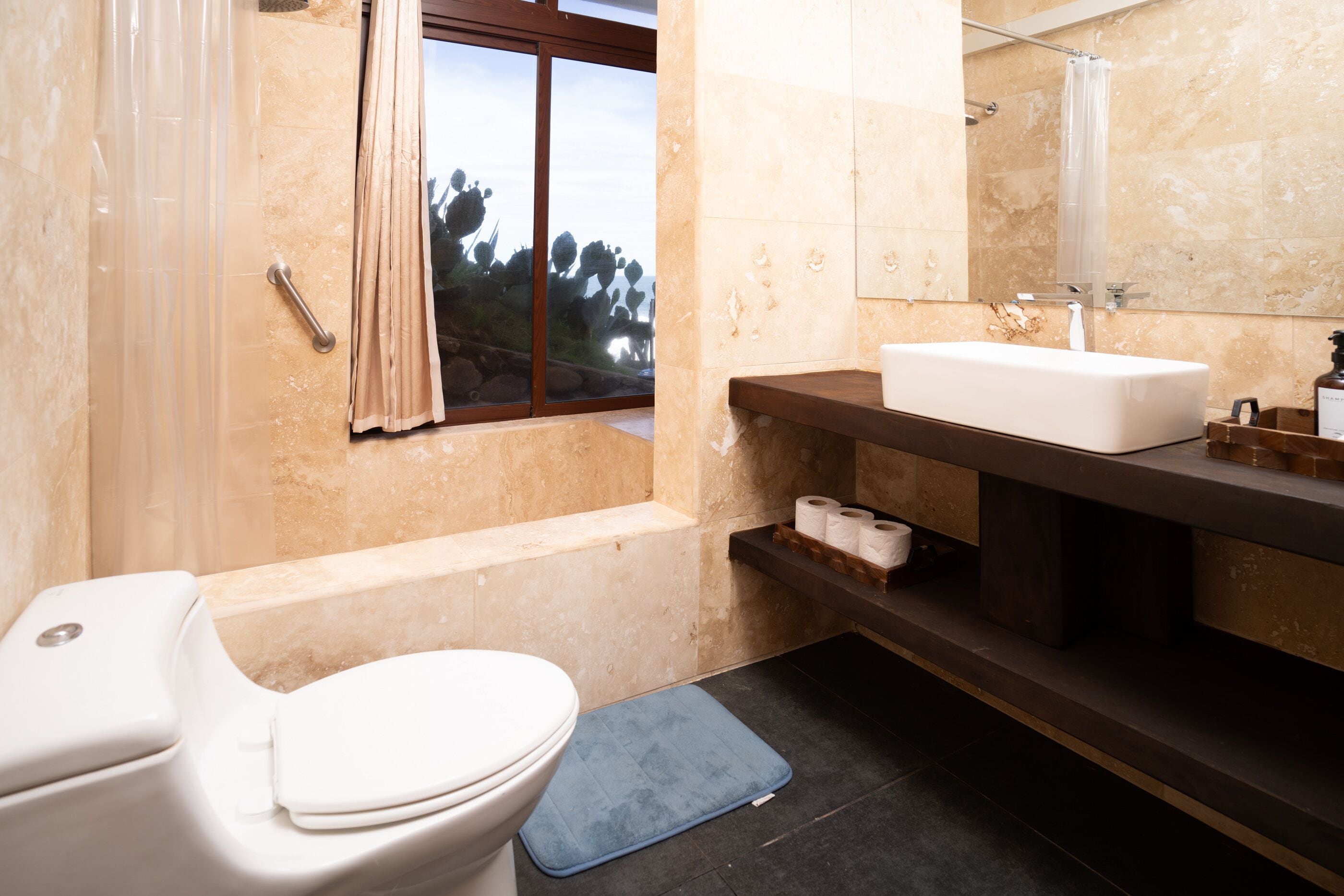 Ein Badezimmer mit Toilette, Waschbecken, Dusche und einem Fenster mit Blick auf Bäume.