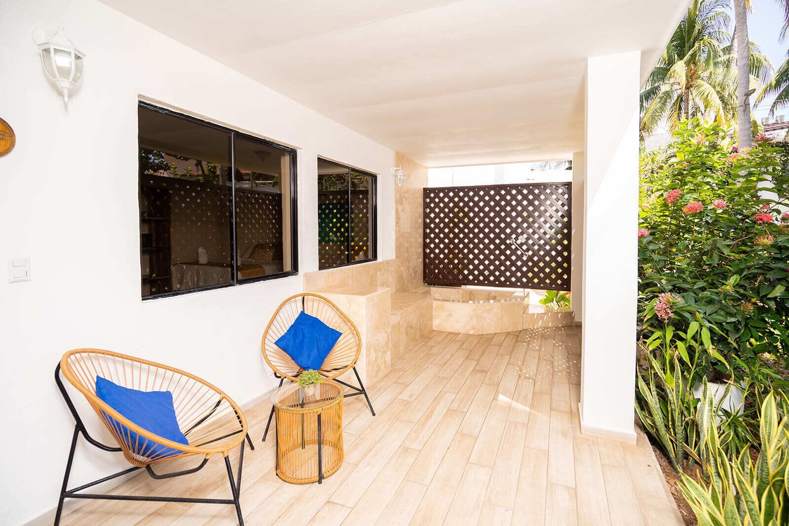 A covered outdoor area with two wicker chairs, a small table, and a decorative wall.