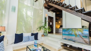 A living room with a white sofa, a glass coffee table, and a flat-screen TV displaying a beach scene. - Royal Palms by Bric (Playa del Carmen)