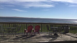 A deck with outdoor seating overlooking a body of water and distant hills. - Carla's Inn (Baraga)