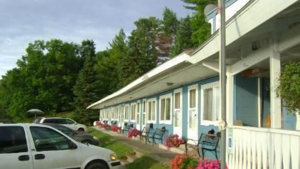 A row of single-story buildings with a row of parked cars in front. - Carla's Inn (Baraga)
