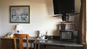 A compact hotel room with a kitchenette, a wooden chair, a framed painting, a television, and a microwave. - Carla's Inn (Baraga)
