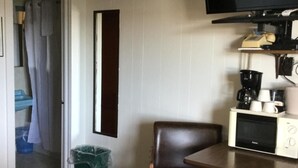 A hotel room with a bed, a TV mounted on the wall, a microwave, a coffee maker, and a chair. - Carla's Inn (Baraga)