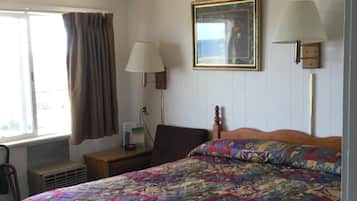 A hotel room with a large bed, a bedside table, a lamp, a picture frame, and a window with curtains.