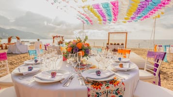 A beachside dining setup with tables, chairs, and a view of the sea.