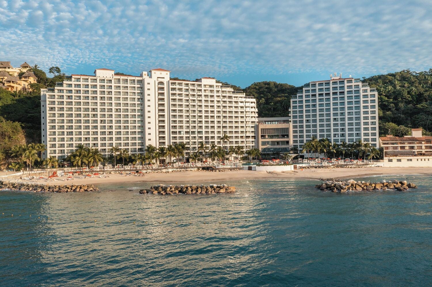 Een strandhotel met meerdere hoge gebouwen, een zandstrand en palmbomen.