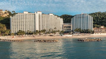 Een strandhotel met meerdere hoge gebouwen, een zandstrand en palmbomen.