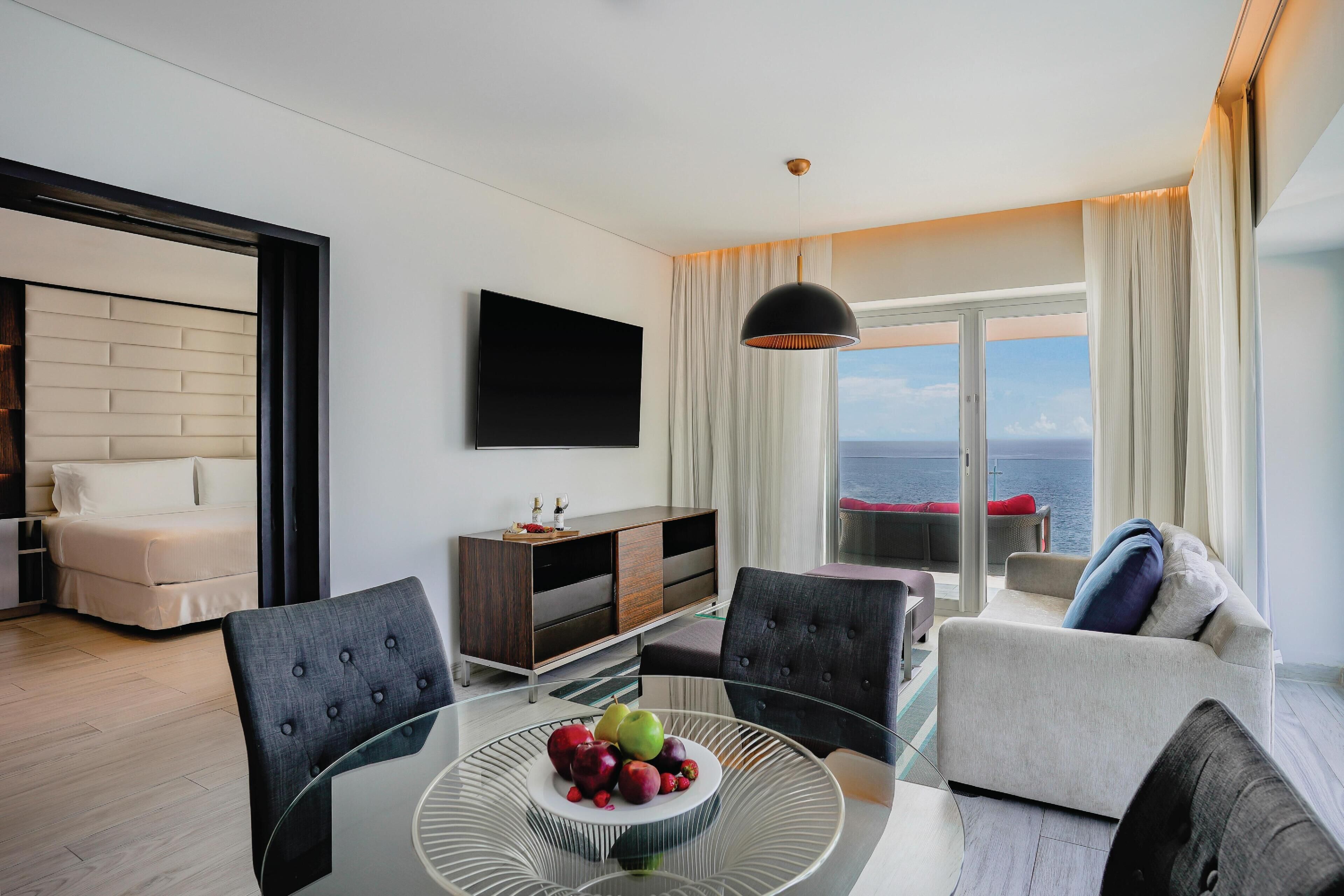 Un salón moderno con una mesa de vidrio, un sofá, un televisor y vista al mar.