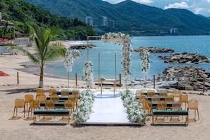 Decoración para una boda en la playa, con un pasillo blanco, sillas y arreglos florales.