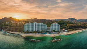 Un hotel con acceso directo a la playa, rodeado de montañas y con zona de piscina.