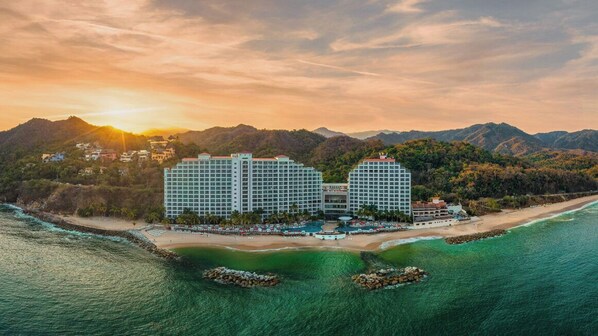 Un hotel con acceso directo a la playa, rodeado de montañas y con zona de piscina.