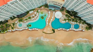 An aerial view of a resort with multiple swimming pools, a beach, and high-rise buildings.