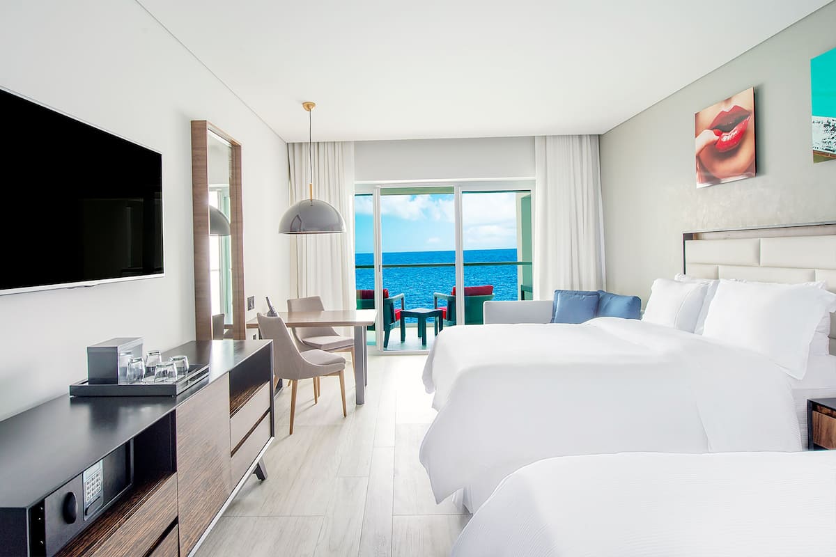 A hotel room with a large bed, a desk with a computer, a TV, and a view of the ocean.