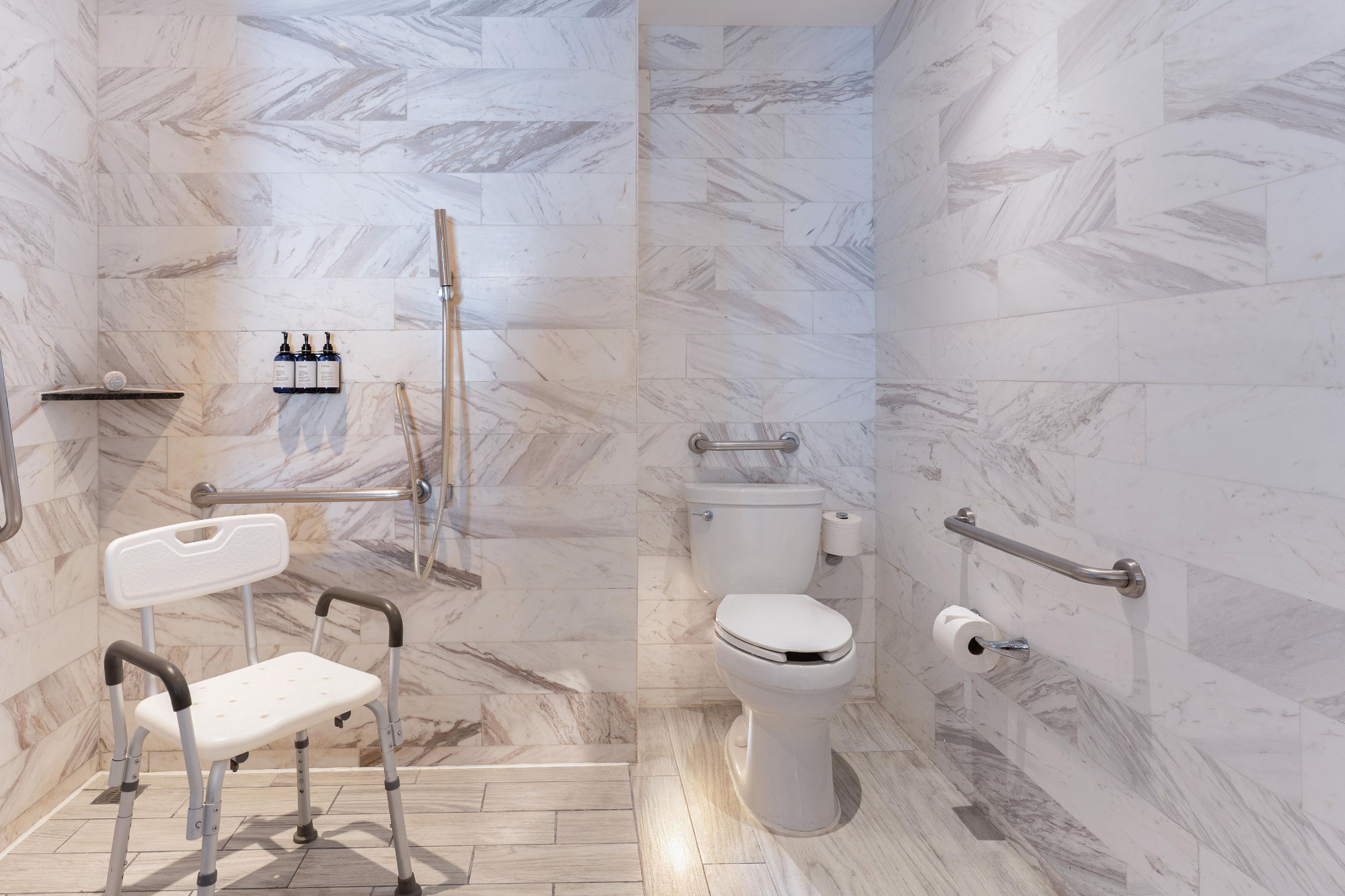 A modern bathroom with a marble floor, a white toilet, a shower area, and a wheelchair-accessible bench.