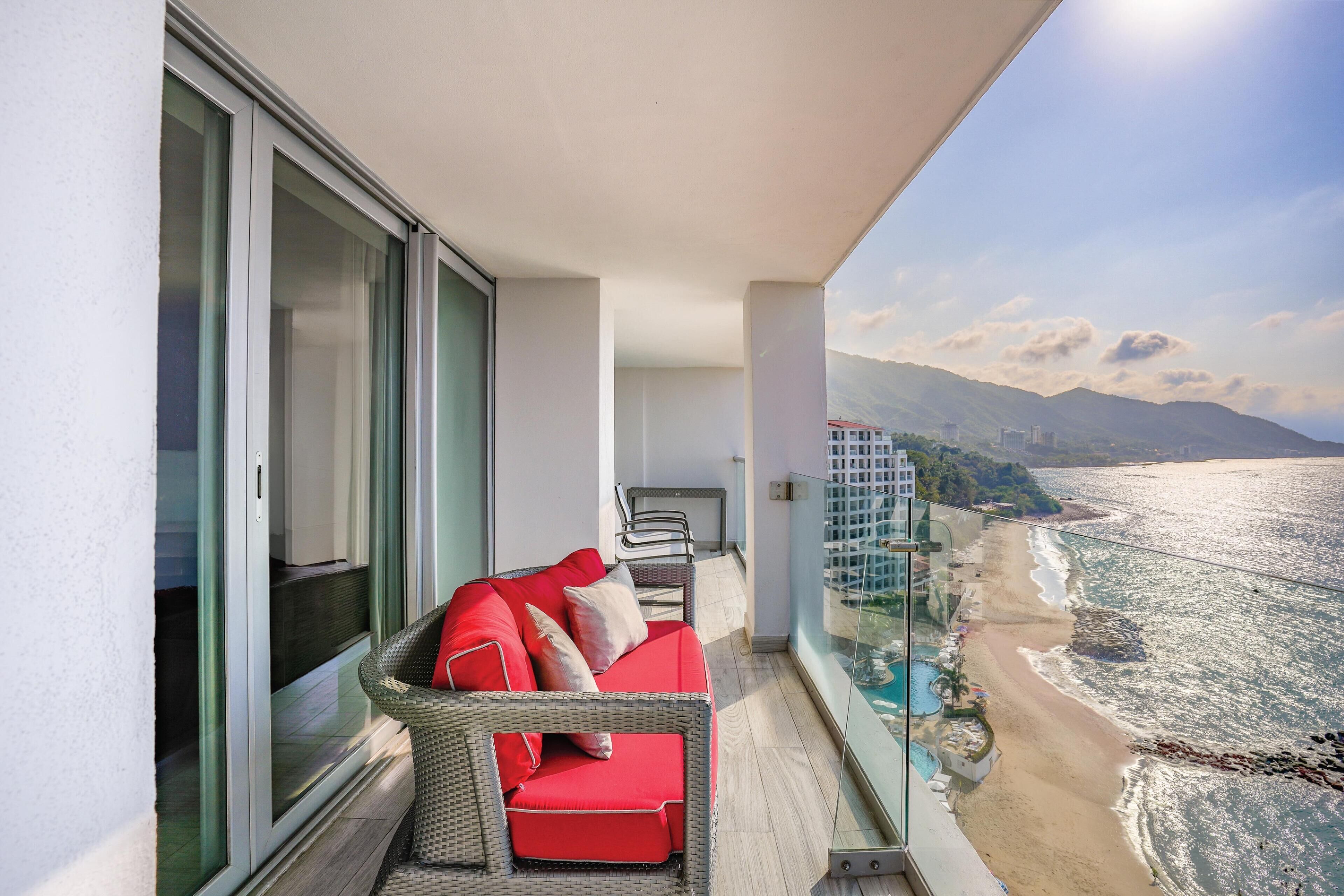 Un balcon avec un canapé, une rambarde en verre et une vue sur la plage et les montagnes.