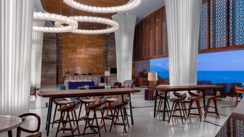 A modern interior with a bar area, seating, and a view of the sea.